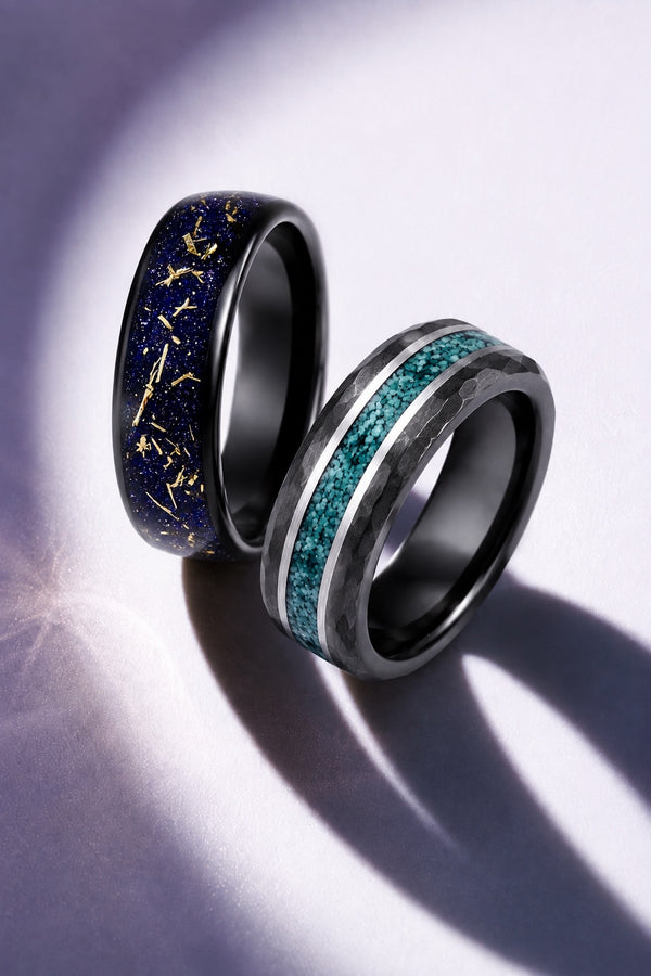 Two men's black wedding bands, one with a blue and gold sandstone inlay and one with a teal stone inlay, on a lilac background, Aquamarise vertical men's ring banner