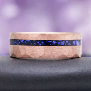 8mm Midnight Blue Sapphire men's wedding band in hammered rose gold tungsten resting on a dark stone, showing the crushed sapphire inlay