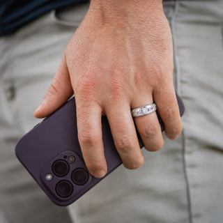 Man wearing the 6mm Moissanite & Amethyst wedding band in sterling silver, bezel-set oval moissanite flanked by amethyst pears and carved leaf shoulders
