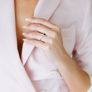 Close-up of a hand wearing a diamond ring with a soft pink background