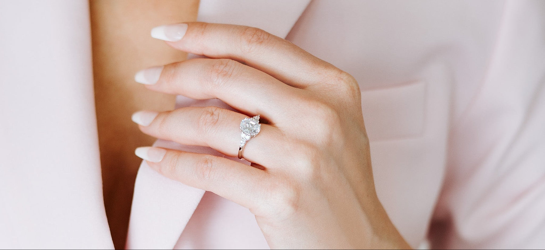 Hand wearing a diamond ring with a soft pink background
