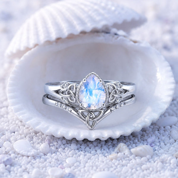 Sterling silver moonstone bridal set with Celtic trinity knot detailing displayed inside a seashell on white sand, Aquamarise collection banner