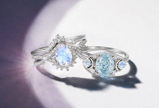 Sterling silver oval moonstone halo ring with a crossover pave band beside an aquamarine ring with crescent moonstone accents in a spotlight on white, Aquamarise banner