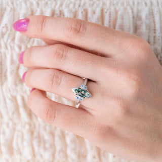 Hand wearing a ring with a green gemstone on a textured white background