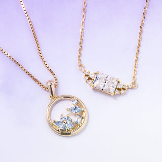 Two gold necklaces with gemstone pendants on a light purple background