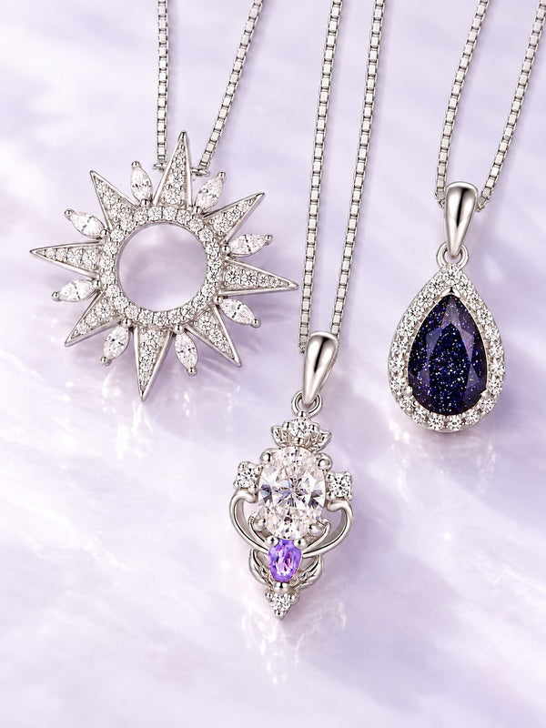 Three silver pendant necklaces on lilac satin: sunburst pendant, oval white pendant with amethyst drop and pear blue sandstone halo pendant, Aquamarise banner