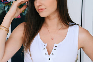 Woman wearing a white sleeveless top with a necklace featuring a red pendant.