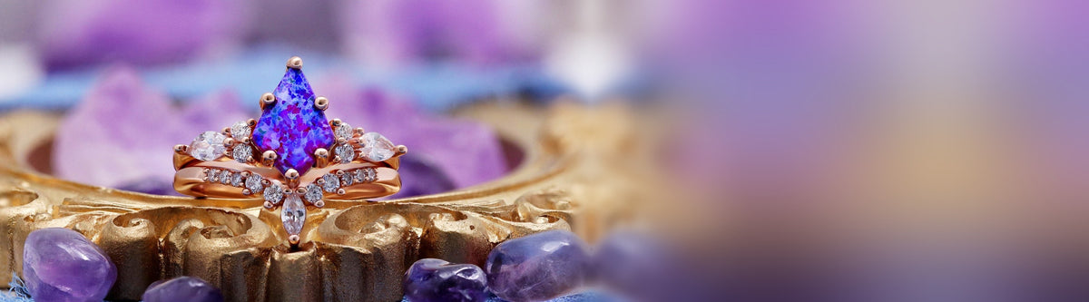 Skye Kite ring set with a lab-created lavender opal on a gold frame beside tumbled amethyst
