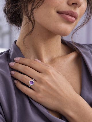 Model in purple satin wearing an oval amethyst halo engagement ring with her hand at her collarbone, Aquamarise amethyst ring portrait banner