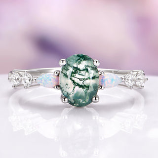 Ring with a green gemstone and opal accents on a white surface with a blurred background