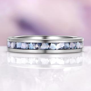 Silver ring with embedded stones on a reflective surface with a blurred purple background