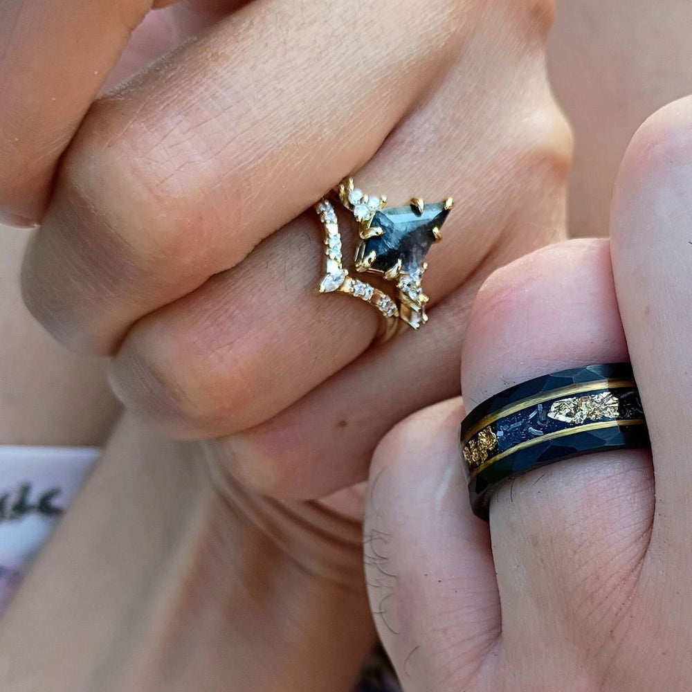 Customer photo of a kite-cut salt and pepper diamond engagement ring in gold beside a black band with gold leaf inlay by Aquamarise