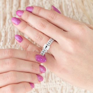 Hand wearing a silver ring with measurement markings on a textured surface