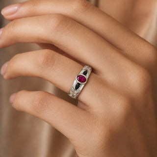 Hand wearing the 6mm Ruby & Black Onyx wedding band in sterling silver, bezel-set oval ruby between two black onyx pears with carved leaf shoulders
