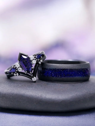 Close-up of two dark rings with glittering deep blue stones and small clear diamonds, resting on a smooth gray surface against a soft purple blurred background.