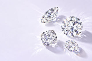 Loose round, oval and marquise cut diamonds scattered on a pale lilac surface catching the light, Aquamarise Sustainability page banner