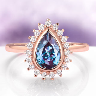 Rose gold ring with a teardrop-shaped blue gemstone and diamond accents on a light purple background.