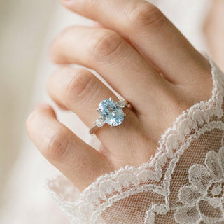 Close-up of a hand wearing a ring with a blue gemstone, wearing a lace sleeve.
