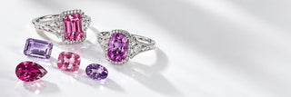 Two white gold halo rings with a pink emerald-cut sapphire and a purple cushion sapphire beside loose pink and purple gemstones on white, Aquamarise Transparency page banner