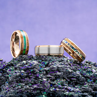 Three gold rings with inlaid stones on a textured surface with a purple gradient background