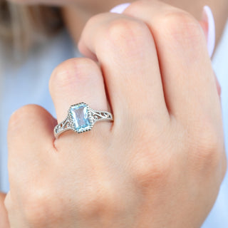 Radiant cut sky blue topaz ring with filigree band worn on a model's hand