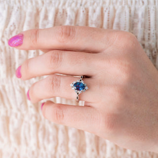 Hand wearing a silver ring with a blue gemstone on a textured beige background