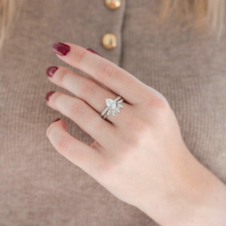 Silver teardrop diamond engagement ring and wedding band on hand over brown background