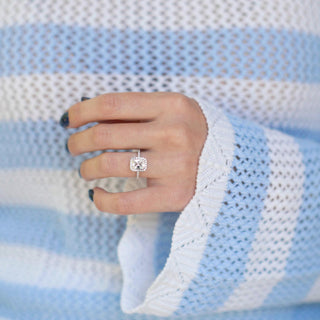 Hand wearing a diamond ring with a blue and white striped sweater background