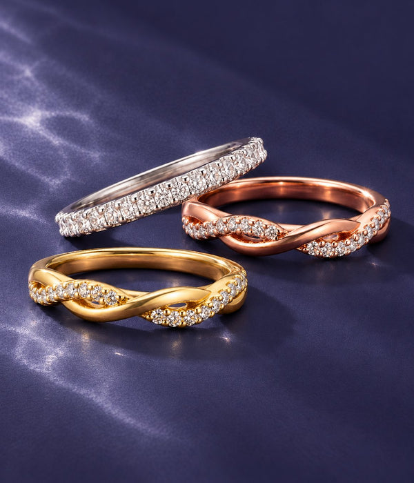 Three women's wedding bands on navy satin: white gold pave eternity band, rose gold twisted pave band and yellow gold twisted pave band, Aquamarise banner